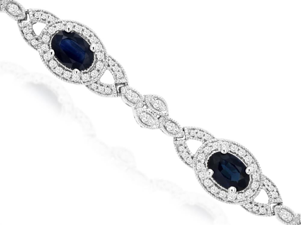 Introducing the Sapphire and Diamond Bracelet by Royal Jewelry: a luxurious silver piece adorned with intricate designs, featuring two large oval-shaped dark blue sapphire gemstones encircled by dazzling white diamonds.