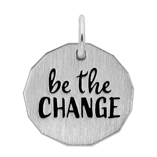 Close-up image of the Be The Change Charm by Rembrandt Charms, crafted from sterling silver in an octagonal shape. The pendant is inscribed with the words "be the CHANGE" in black, cursive and bold letters. This charm features a small loop at the top for attaching to a chain or cord.