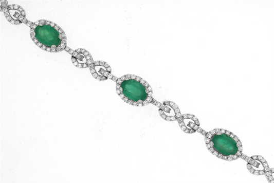 The Royal Jewelry emerald and diamond bracelet, Style #WH1074E, features four oval green gemstones encircled by small diamonds and linked with 14K white gold diamond-encrusted infinity symbols. It's elegantly displayed against a plain white background.