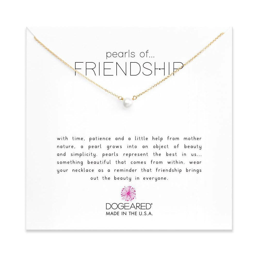 A gold chain necklace, 18" long, featuring a single pearl pendant is showcased against a white background. The card behind the necklace reads "Pearls of Friendship" and includes a sentiment about the beauty of both friendship and pearls. This elegant piece is from the brand Dogeared, made in the USA.