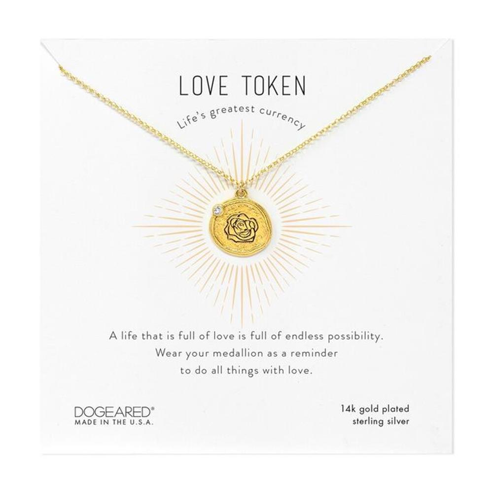 A gold necklace from the brand Dogeared features a circular "Love Token" Rose pendant with a rose design. The 18-inch necklace, made of 14k gold plated sterling silver and crafted in the U.S.A., is displayed on a card that reads, "LOVE TOKEN - Life's greatest currency" and includes an inspirational message.