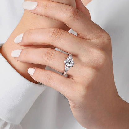 A hand with neatly manicured nails wears the exquisite 14K Gold Oval Diamond Engagement Ring by Gabriel & Co, featuring a large, sparkling diamond set in a sleek white gold band against a white fabric background.