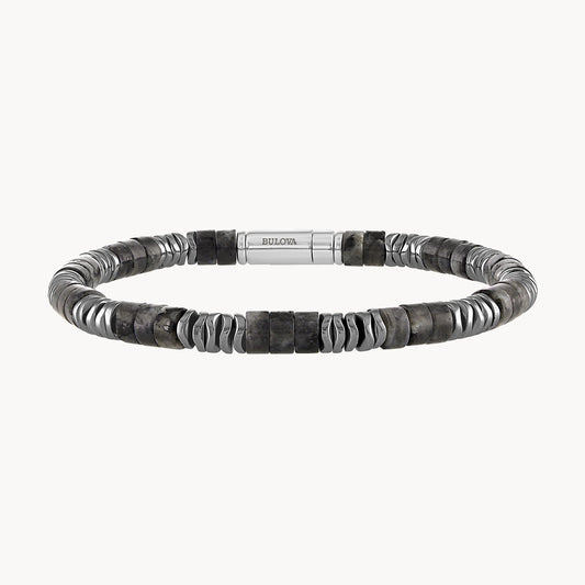 The Labradorite and Hematite Beaded Bracelet from Bulova Watch Company features a sleek, minimalist design with alternating silver and dark grey beads. It is adorned with Labradorite beaded accents and has a central sterling silver clasp engraved with the Bulova logo. The bracelet is crafted using a mix of smooth cylindrical and irregularly shaped beads.