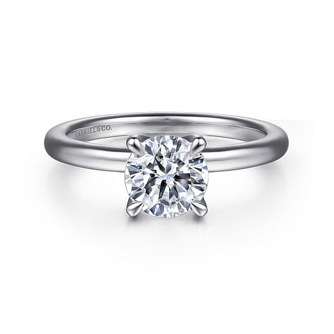 An elegant solitaire engagement ring with a round brilliant-cut diamond set in a classic four-prong setting on a polished 14K white gold band. The word "Gabriel & Co" is engraved on the inside of the customizable engagement ring.