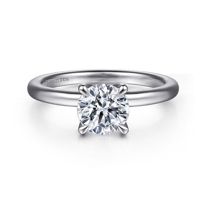 An elegant solitaire engagement ring with a round brilliant-cut diamond set in a classic four-prong setting on a polished 14K white gold band. The word "Gabriel & Co" is engraved on the inside of the customizable engagement ring.