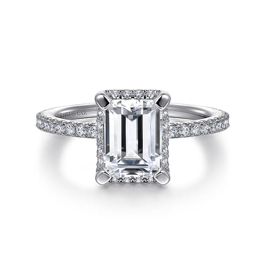 This exquisite engagement ring from Gabriel & Co's Classic Collection features a prominent emerald-cut diamond at its center, surrounded by a halo of smaller round diamonds. Crafted from 14K white gold, the elegant band is adorned with shimmering round diamonds.