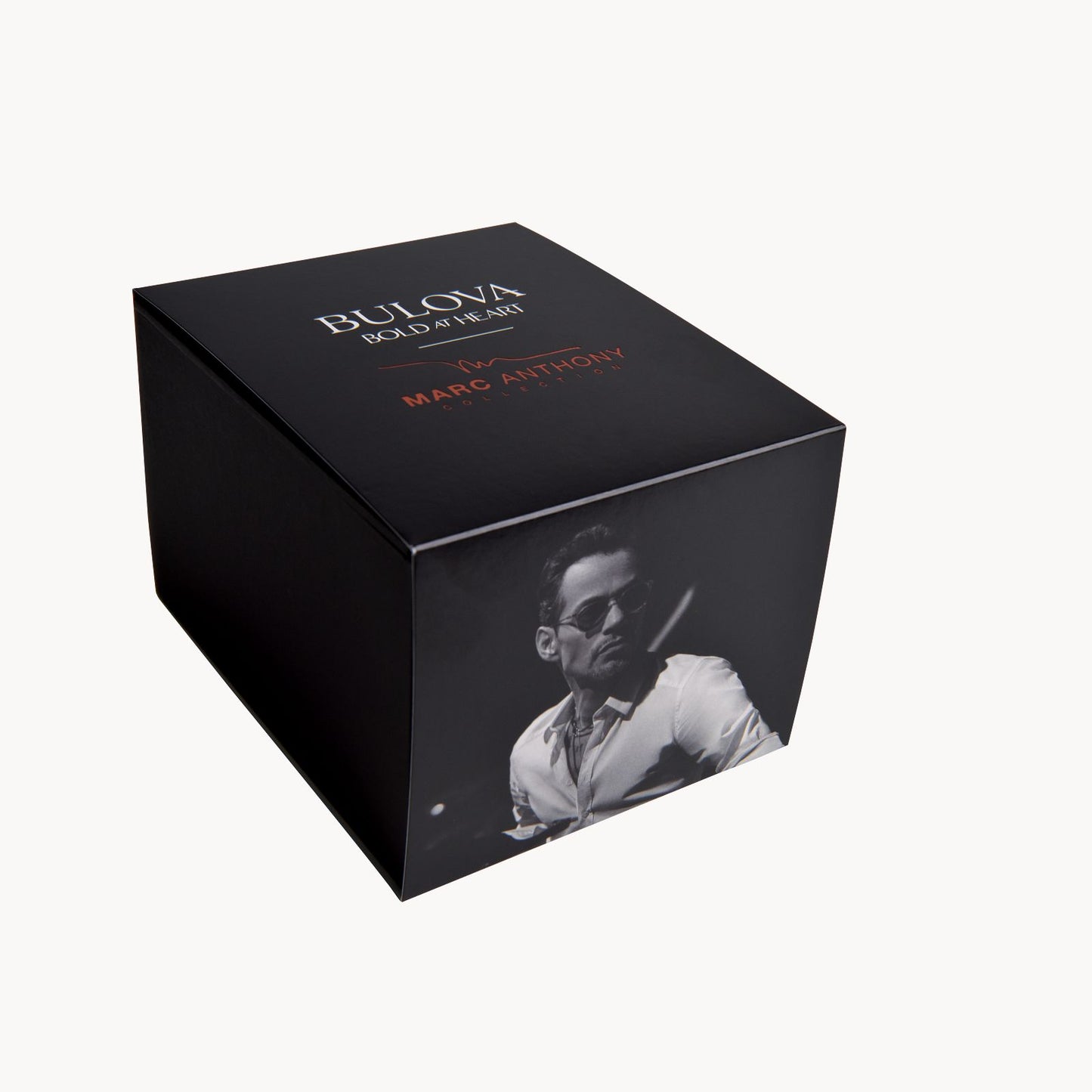 A black box for the Marc Anthony Marine Star Watch by Bulova Watch Company featuring "Bold at Heart" branding and a photo of a man wearing sunglasses and a white shirt. The names "Marc Anthony" and "Bulova" are printed on the box in white and orange text, highlighting the elegant diamond accents of the Marc Anthony Marine Star Watch collection.