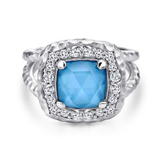 The Gabriel Sterling Silver Turquoise Ring by Gabriel & Co showcases a square-cut turquoise gemstone surrounded by small clear crystals. The band exhibits a textured, braided design that enhances the intricate and elegant setting of the vibrant central stone.