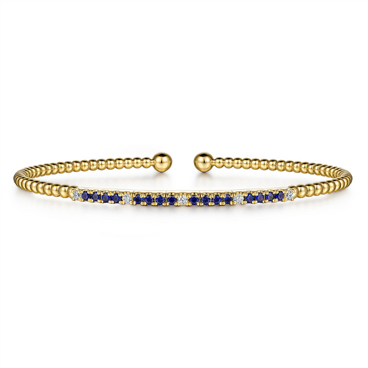 Introducing the Gabriel & Co. 14KY Bujukan Diamond and Blue Sapphire Split Bangle (SN: S1955564). This delicate gold bangle bracelet features small, round beads along its band and an open cuff design with two spherical ends. The centerpiece is adorned with alternating blue sapphires and white gemstones.