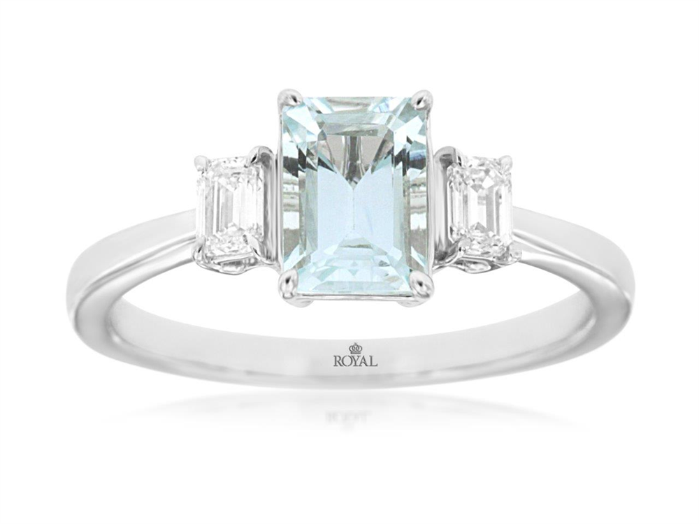 A stunning 14K white gold engagement ring from Royal Jewelry, Style # WH2016Q, features an emerald-cut aquamarine at the center accented by two smaller rectangular diamonds. The sleek and polished band discreetly bears a subtle logo on the inner side, embodying timeless elegance and sophistication.