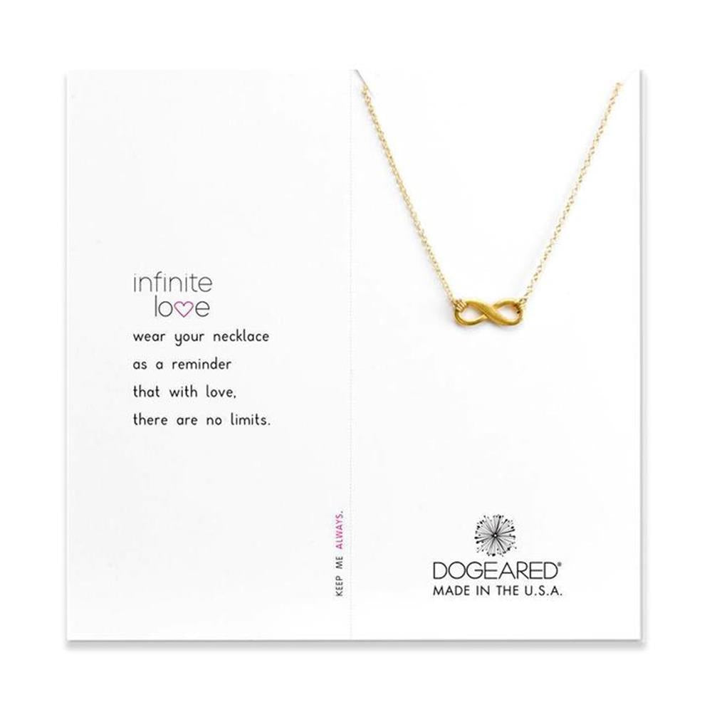 A gold Dogeared Infinite Love necklace with an infinity symbol pendant is displayed on a white card. The card reads: "Infinite love. Wear your necklace as a reminder that with love, there are no limits." The corner of the 16" necklace with a 2" extender states: "DOGEARED MADE IN THE U.S.A.