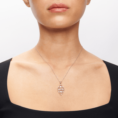 A person wearing a black, square-neck top is shown from the chin to the collarbone, highlighting a Simon G. 18K Two-Tone Gold Lacework Diamond Pendant with an intricate geometric design. The background is white, focusing attention on the necklace.