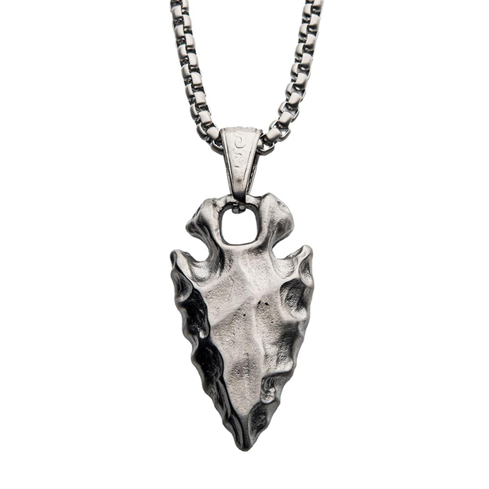 The Brushed Steel Chiseled Arrowhead Pendant with Box Chain by INOX features a silver arrowhead pendant with detailed, rugged edges and a small hole near the top for attachment, giving it an antiquated and handcrafted appearance. The pendant hangs from a sturdy, textured box chain.