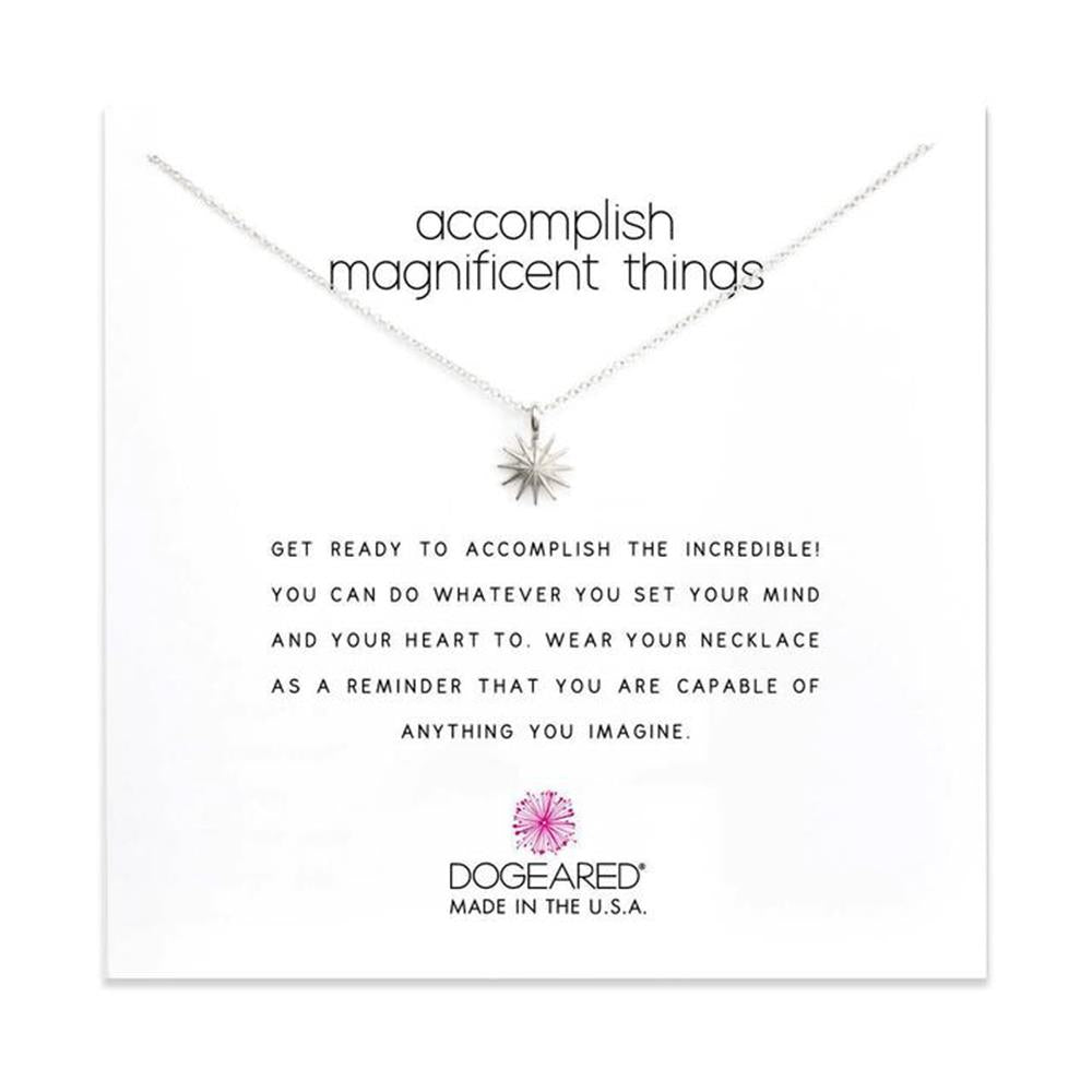 An elegant silver necklace, part of Dogeared's "Accomplish Magnificent Things" collection, features a small starburst pendant. The text above the necklace reads, "Accomplish magnificent things." Below are inspirational words encouraging the wearer to achieve their dreams, proudly attributed to DOGEARED, MADE IN THE U.S.A.