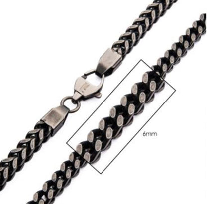 A close-up view of the 6mm Oxidized Steel Franco Chain by INOX showcases its intricate interlocking design, blending black and silver accents. The men's necklace, measuring 20 inches in length and crafted from durable stainless steel, features a secure lobster clasp fastening.