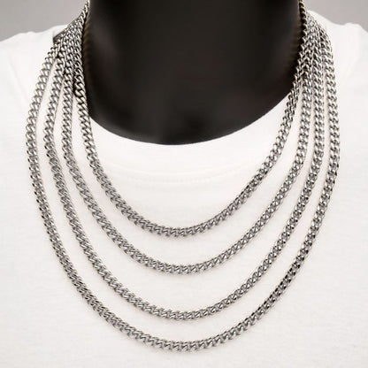 A person wearing multiple layered necklaces, including the bold 6mm Steel Miami Cuban Chain by INOX, over a white shirt. The men's necklaces are displayed evenly across the chest, creating a cascading effect. The background is neutral, focusing attention on the jewelry.