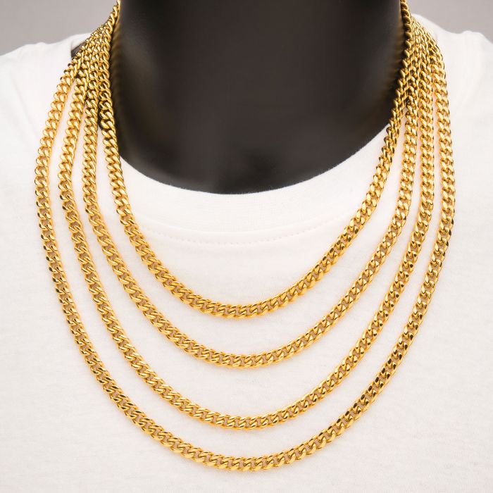 A close-up image of a person wearing a white shirt and multiple 6mm 18K Gold Plated Miami Cuban Chains from INOX. The men's necklaces are thick and arranged in layers, draping over the chest, creating a luxurious and striking appearance. The person's face is not visible in the image.