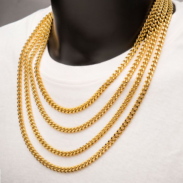 A person wearing five INOX 6mm 18K Gold Plated Miami Cuban Chains, each 22" long, layered over a white shirt. The chains showcase a uniform, thick design, exuding boldness and luxury. The neutral background accentuates the prominent men's necklaces.