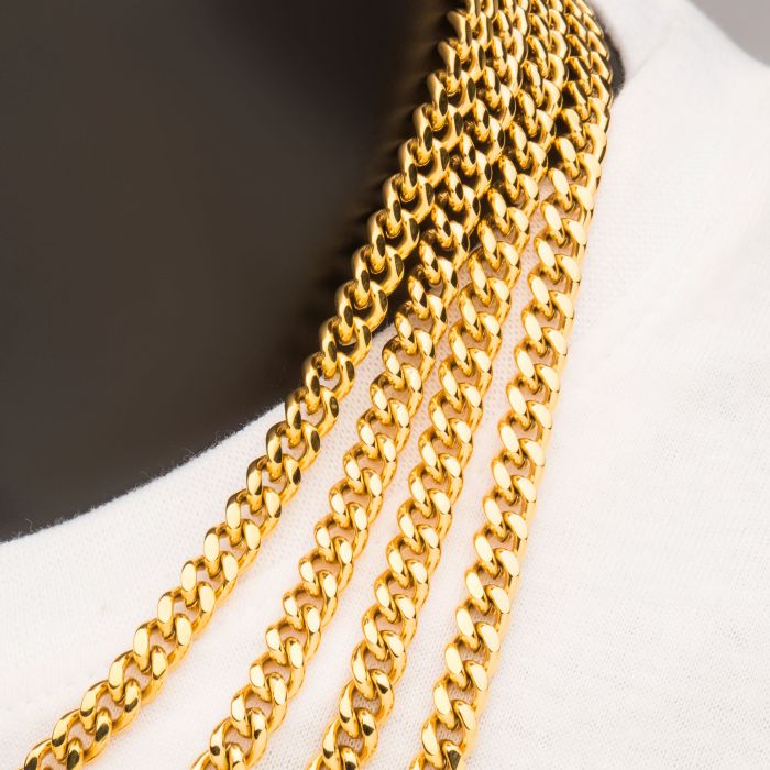 Close-up of a person wearing multiple INOX 6mm 18K Gold Plated Miami Cuban Chains, each 20 inches in length. The glossy gold chains are layered over a white garment, standing out prominently against a dark background.