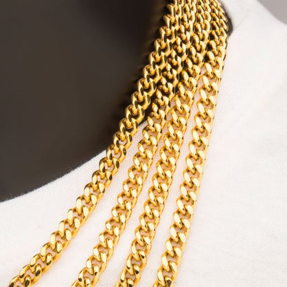 A close-up view of a person wearing multiple overlapping 6mm 18K Gold Plated Miami Cuban Chains by INOX on a white shirt. The chains have a polished, reflective surface and a classic curb link design, creating a layered, luxurious look.