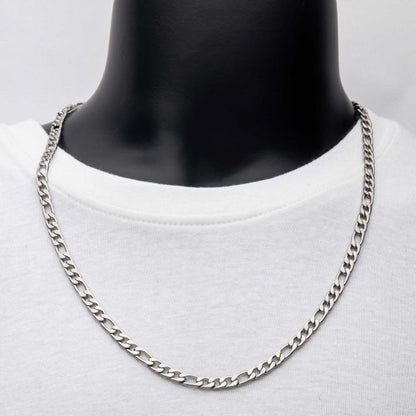 A close-up shot of a person wearing a white t-shirt, showcasing the INOX 6mm Steel Figaro Chain (22") around their neck. The background is plain, emphasizing the chain's detailed design and shiny finish. The person's head and lower body are not visible.