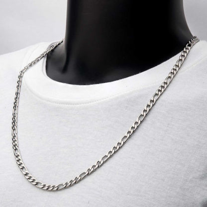 A close-up image of a person wearing a white shirt and the 6mm Steel Figaro Chain from INOX. The men's stainless steel necklace, measuring 22 inches, features a simple, elegant design with closely linked metal segments, resting against the person's collarbone and neckline. The background is plain and unobtrusive.