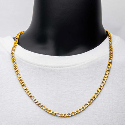 A close-up view of a person wearing the 6mm 18K Gold Plated Figaro Chain by INOX, draped over a plain white shirt. The chain, which measures 20 inches and features a classic curb link design, rests evenly around the neck against a solid gray background.