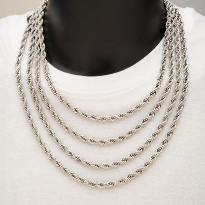 A close-up of a person wearing a white shirt with five layered INOX 6mm Steel Rope Chains displayed around their neck. The stainless steel chains, each measuring 22", vary slightly in length, creating a cascading effect. The plain background emphasizes the intricate details of the chains.