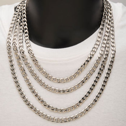 A close-up image of a person wearing multiple men's necklaces, including a stylish 8mm Steel Bevel Curb Chain by INOX and a sleek stainless steel chain, each with different lengths, arranged to layer on top of a white shirt. The background and the person’s features are not visible, only the neck and part of the chest.