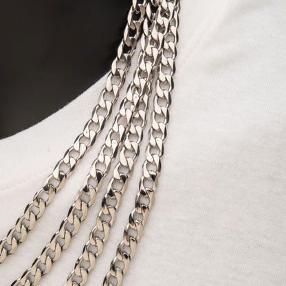 Close-up shot of several INOX 8mm Steel Bevel Curb Chains draped over a white fabric. The 20" bevel curb chain from INOX features a detailed, interlocking pattern that reflects light subtly, accentuating its metallic sheen against the contrasting fabric background.