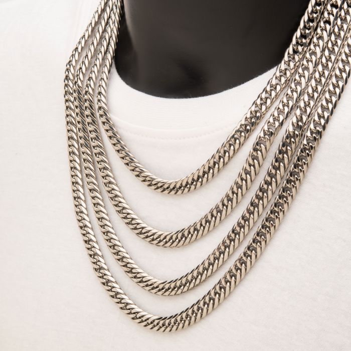 Close-up of a person wearing a white shirt and layered silver chains, including the 8mm Steel Dome Curb Chain by INOX. The men's necklaces are of varying lengths, draping in a cascading effect around the neck. The pendants or additional details, if any, are not visible in the image.