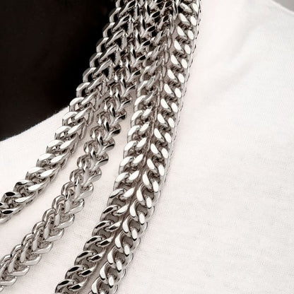 Close-up of multiple silver chains placed against a white fabric backdrop. The robust, interwoven design of the 6mm Steel Franco Chain | 20" | INOX shines and reflects light beautifully, highlighting the elegant craftsmanship typical of a men's stainless steel necklace from INOX.