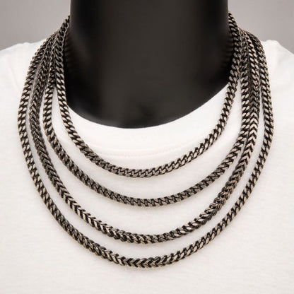 A white mannequin torso is adorned with a 6mm oxidized steel Franco chain necklace from INOX, measuring 20 inches. The men's necklace features the signature Franco chain elements, exhibiting a polished and slightly oxidized finish that creates a striking contrast against the white top.