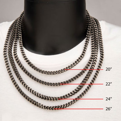 A display features a black mannequin adorned with four INOX 6mm Oxidized Steel Franco Chains of varying lengths on a white shirt. The men's necklaces are labeled with their lengths: 20 inches, 22 inches, 24 inches, and 26 inches.