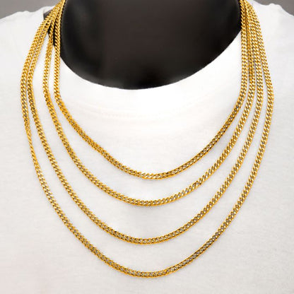 A close-up photo of a person wearing a white shirt and five layered 6mm 18K gold plated diamond cut curb chains by INOX. The chains, which may be men's necklaces, are of varying lengths and have a shiny, polished appearance, creating a cascading effect across the chest. The person’s face is not visible in the image.