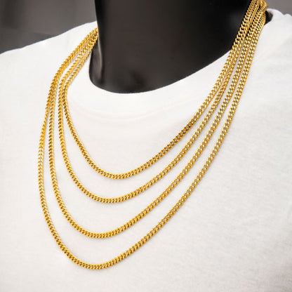 Close-up of a person wearing a white shirt, showcasing four INOX 6mm 18K Gold Plated Diamond Cut Curb Chains of varying lengths, arranged in a cascading layer. The background is neutral, emphasizing the bright and shiny appearance of the stainless steel necklaces.