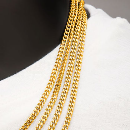 A close-up image features multiple 6mm 18K Gold Plated Diamond Cut Curb Chains by INOX, elegantly draped around the neck of a person wearing a white shirt. The details of these 24-inch chains and how they gracefully lay over the fabric are highlighted against a dark background.