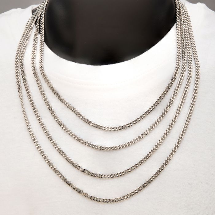 A person wearing a plain white shirt and the INOX 8mm Diamond Cut Curb Chain Necklace, a multi-layered men's stainless steel accessory that drapes elegantly over the chest. The 24" necklace consists of five evenly spaced diamond cut curb chains, creating a stylish and sophisticated look against the white fabric.