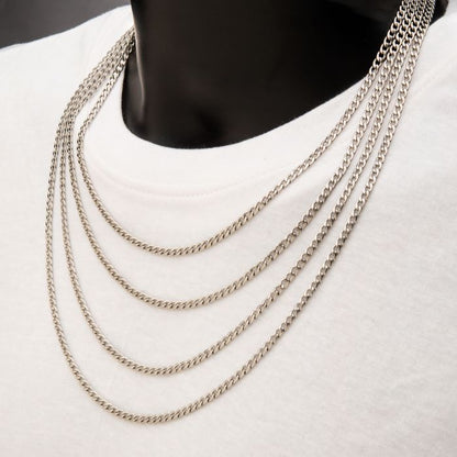 A person wearing a white t-shirt is accessorized with five layered INOX 4mm Steel Classic Curb Chain necklaces of varying lengths. The sleek, consistent link pattern of each 20" necklace drapes elegantly down the front, set against a neutral background that emphasizes the jewelry.