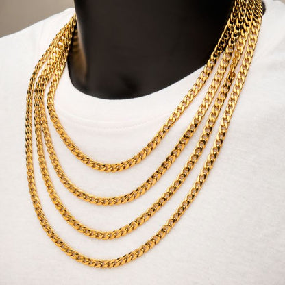 A close-up shot features a person wearing a white shirt embellished with six layers of the 4mm 18K Gold Plated Classic Curb Chain by INOX, each chain measuring 24 inches. The chains are meticulously spaced and elegantly drape over the chest, highlighting their intricate link design. The person's face is not visible in the image.