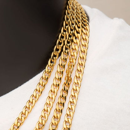 Close-up of a person wearing multiple gold chains, including the 6mm 18K Gold Plated Classic Curb Chain by INOX, around their neck over a white garment. The neutral background enhances the focus on the brightly shining gold chains.