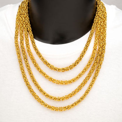 A person wearing a white shirt and four layers of INOX 6mm 18K Gold Plated King Byzantine Chain necklaces around their neck. The gold chains are thick and ornate, creating a luxurious and elegant appearance.