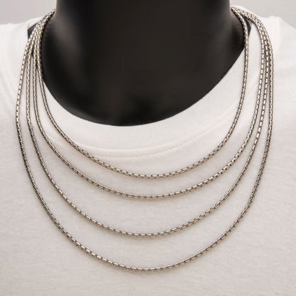 A close-up of a person wearing a plain white shirt, showcasing five layered 3mm Steel Boston Link Chains by INOX resting above the neckline. The background and other details of the person are not visible.