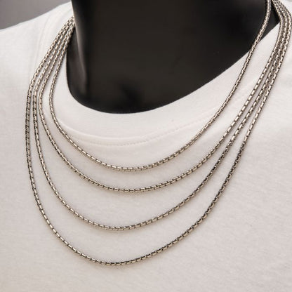 Close-up of a person wearing a white t-shirt and four 3mm Steel Boston Link Chains from INOX around their neck. The chains have a sleek Boston link design, creating an elegant appearance against the plain white background of the shirt. The stainless steel chains pop against the neutral, unobtrusive backdrop.