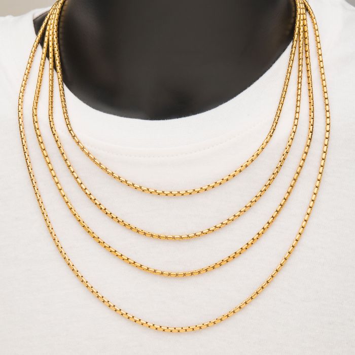 A close-up of a mannequin wearing a white top adorned with four layered INOX 3mm 18K Gold Plated Boston Link Chain Necklaces, each measuring 20 inches in length. The chains are evenly spaced and feature a delicate, intricate design.