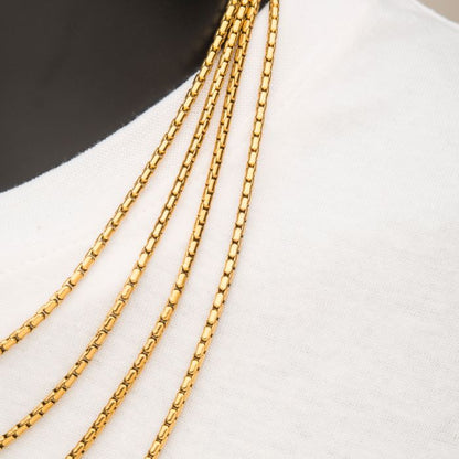 Close-up of a person wearing a white shirt with four 3mm 18K Gold Plated Boston Link Chain Necklaces by INOX resting on their chest. The men's necklaces have a shiny, elegant appearance and are layered one above the other. The neutral background emphasizes the details of the jewelry and fabric.