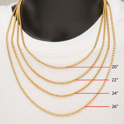 A black mannequin is showcasing four men's 3mm 18K gold-plated Boston Link Chains (20 inches, 22 inches, 24 inches, and 26 inches) from the INOX brand. The layered necklaces are elegantly draped over a white garment, with red lines and labels indicating the lengths of each stainless steel chain.