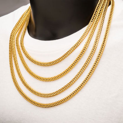 A mannequin displays multiple layers of INOX's 6mm 18K Gold Plated Foxtail Chains resting on a white shirt. The 18K gold-plated chains are intricately crafted with a herringbone pattern, creating a layered, elegant look.