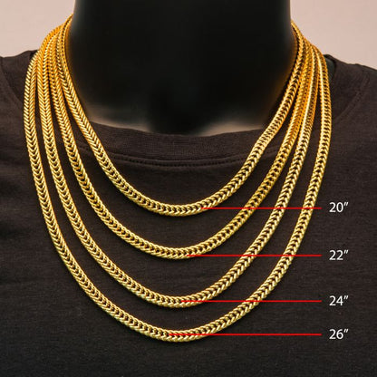 A person wearing a black shirt showcases five gold chain necklaces of varying lengths. One of the necklaces is the 6mm 18K Gold Plated Foxtail Chain by INOX, measuring 20 inches. The lengths of the other chains are marked with red lines and text: 22 inches, 24 inches, and 26 inches.