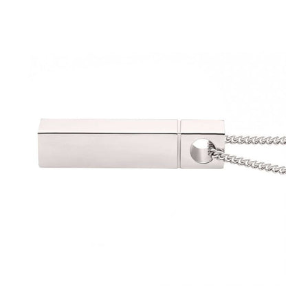 A sleek, rectangular silver pendant from the "The Keepsake Urn Engravable Pendant with Chain" by INOX is laid horizontally on a white background. The pendant has a smooth, minimalist design with no visible markings or logos and is attached to a 925 Sterling Silver chain. The cap is partially removed, revealing the USB connector.